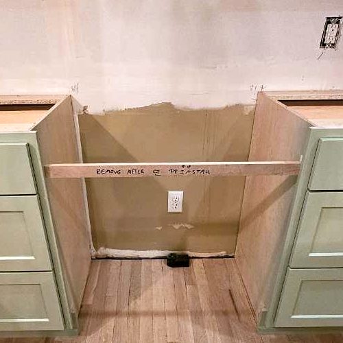 Temporary brace across a range opening, hand-marked to be removed after countertop install