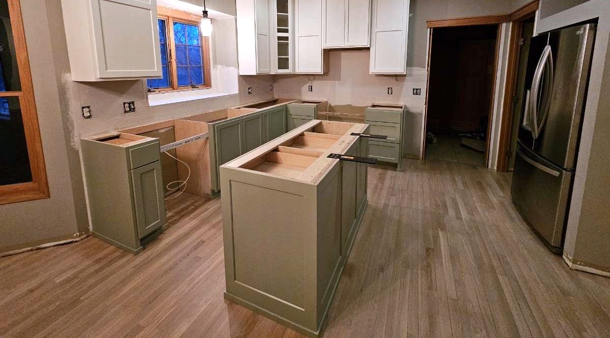 Sage green base cabinets and island with white upper cabinets, set in place during installation