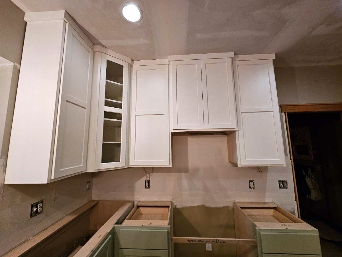 White shaker upper cabinets with a glass-front corner cabinet and crown, above sage green drawer bases